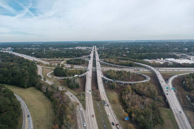 Aerial view of a wide highway corridor through wooded suburbs