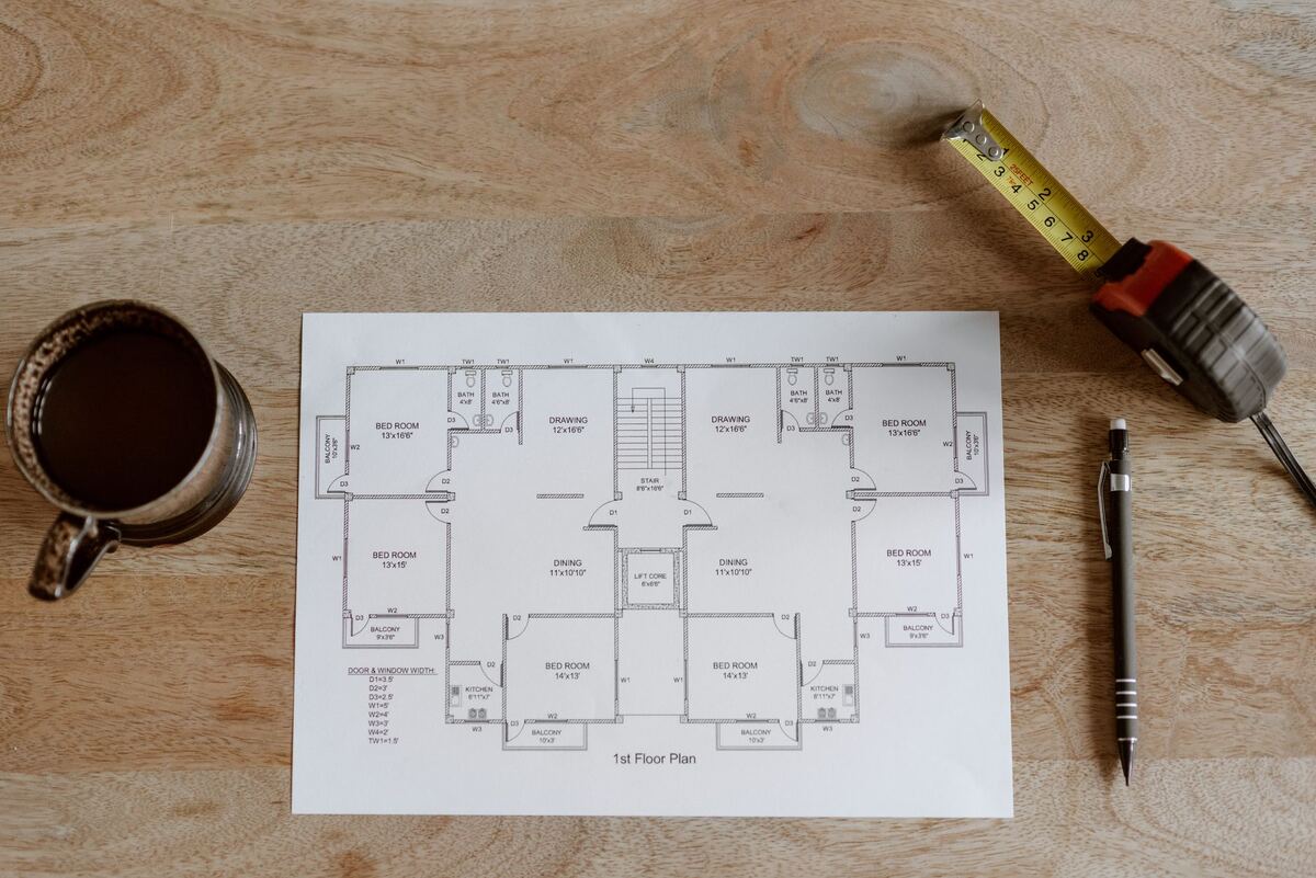 Printed floor plan beside a tape measure on a wooden table