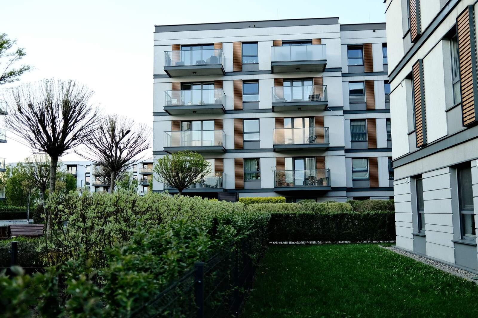 Apartment buildings behind a clipped hedge and a landscaped lawn