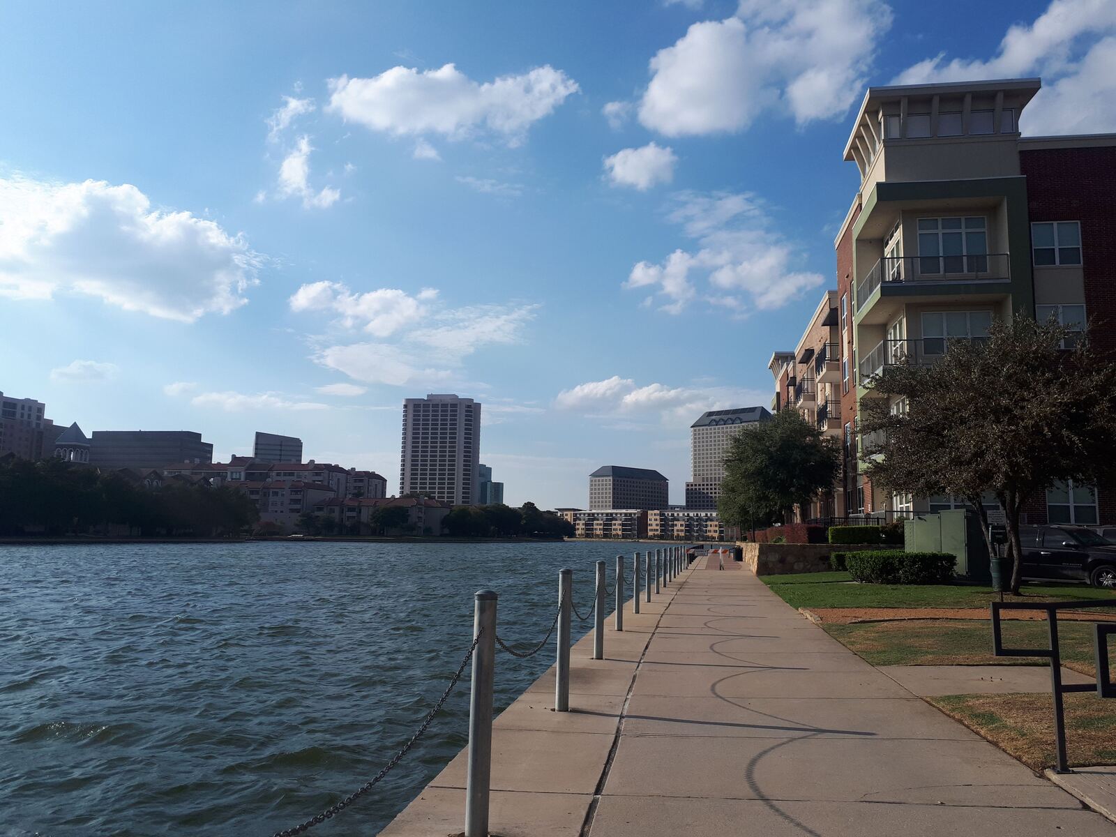 Paved waterside path beside apartment buildings and a city skyline